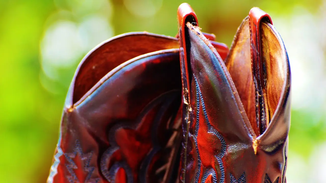 Częściowo widoczne buty kowbojskie, błyszczące fragmenty skóry o intensywnym czerwono-brązowym odcieniu